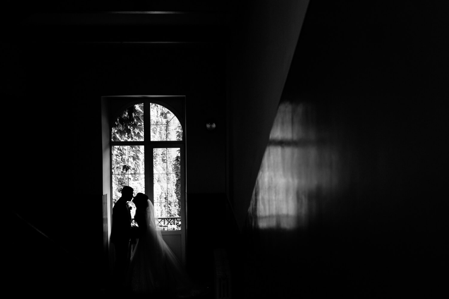 monochrome view silhouette wedding couple which is nearly kissing near window